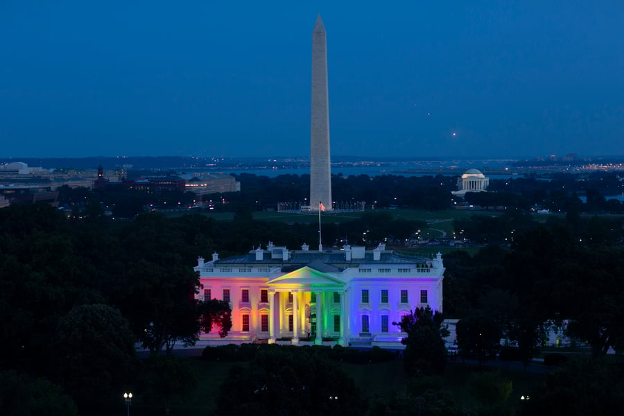 Photograph of the White House in Washington DC at dusk lit with rainbow colors. The Washington Monument stands in the background.
