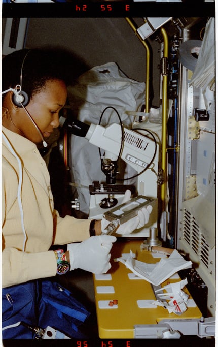 Side profile photograph of a woman astronaut looking into a microscope