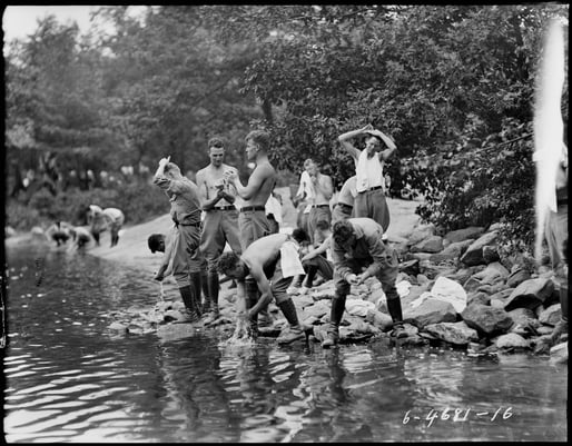 Black and white photograph of a group of soldiers standing on a riverbank, washing up.