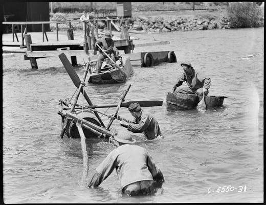 Black and white photograph of a group of soldiers standing waist deep in the water, moving equipment and boats. 