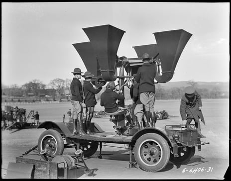 Black and white photograph of soldiers standing on a vehicle platform with funnel shaped devices facing up to the sky.