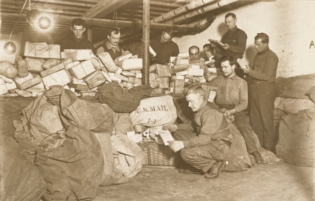 Black and white photograph of men surrounded by bags of mail and reading letters