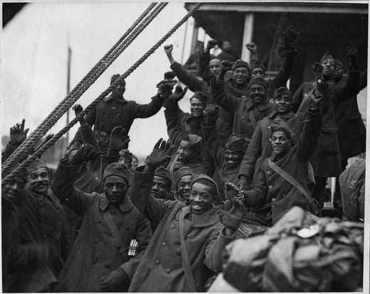 Black and white photograph of group of soldiers waving at the camera from aboard a ship