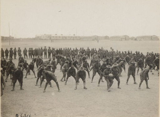 Black and white photograph of a group of military servicemembers in the middle of a game of hidden ball. Man in the front has the ball while the others look around