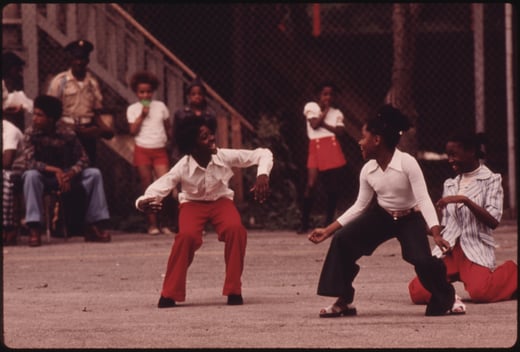 Photograph of two young girls dancing in the street while other watch from the background