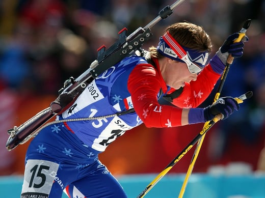 Biathlon competitor skis during competition with her rifle slung across her back.