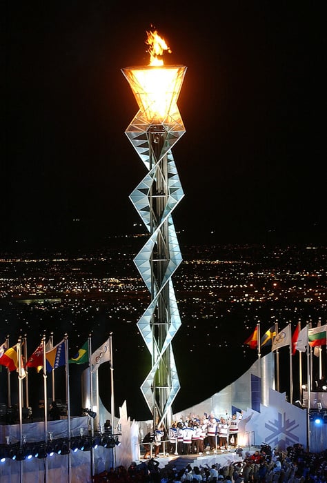 Olympic flame from the opening ceremonies in Salt Lake City. It is nighttime, and the lights of the city can be seen in the distance behind the flame