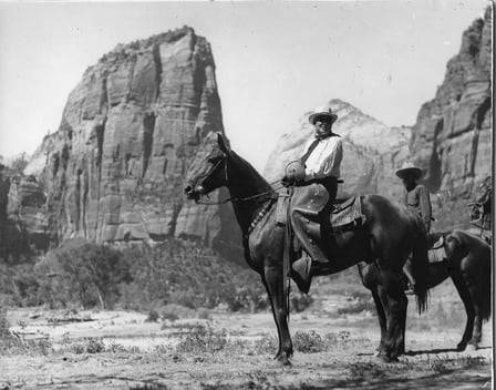 Black and white photograph of President Warren G. Harding on horseback. The mountains of Zion National Park are in the background. 