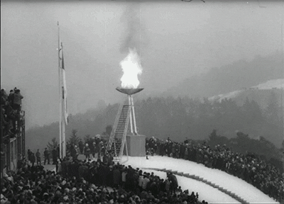 Animated GIF of the Olympic Flame with spectators along both sides. Mountains and snow surround the flame.