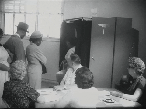 Black and white animated GIF of voters standing in line and entering and exiting a voting booth while poll workers sitting at a table look on. 