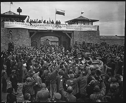 Liberated prisoners in the Mauthausen concentration camp near Linz, Austria, give rousing welcome to Cavalrymen of the 11th Armored Division. The banner across the wall was made by Spanish Loyalist prisoners.