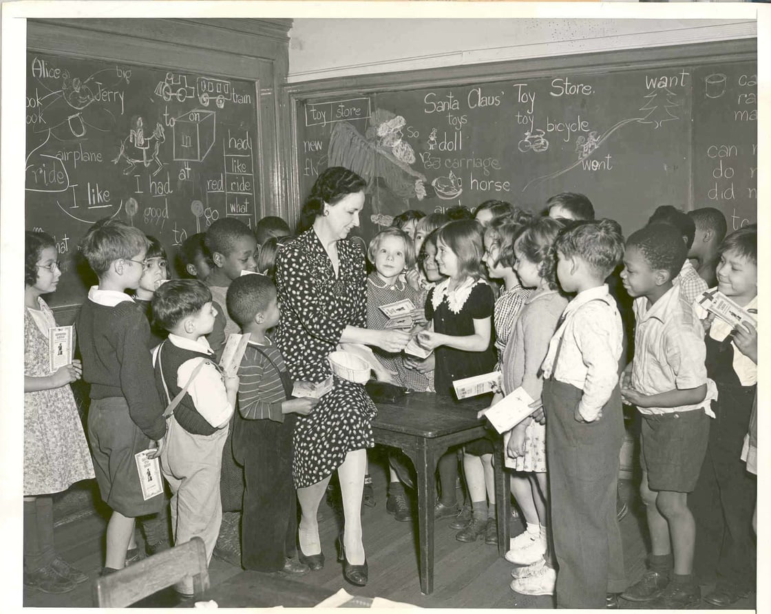This photograph shows students in Miss Mary O’Donne’s 1st grade class at P.S. 56 in New York City buying war bonds and stamps during the Fourth War Loan Drive.